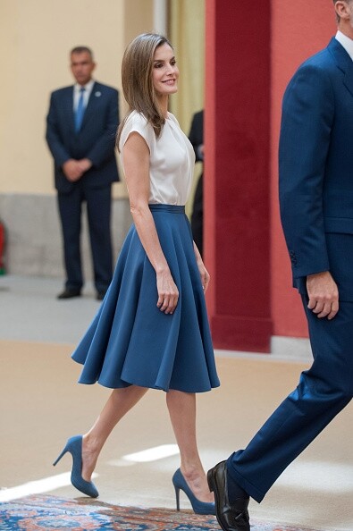 Queen Letizia穿搭米白色絲質上衣，下身配搭藍色中長裙及高跟鞋，傘裙款式除了