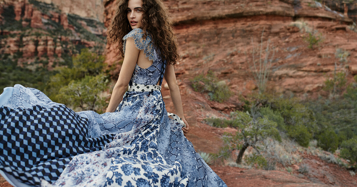 藍色主調的印花圖案長裙，蛇紋與花卉圖案交錯，裙擺於風中搖曳生姿，揚
